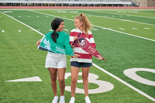 Two girls standing on football field with school flags