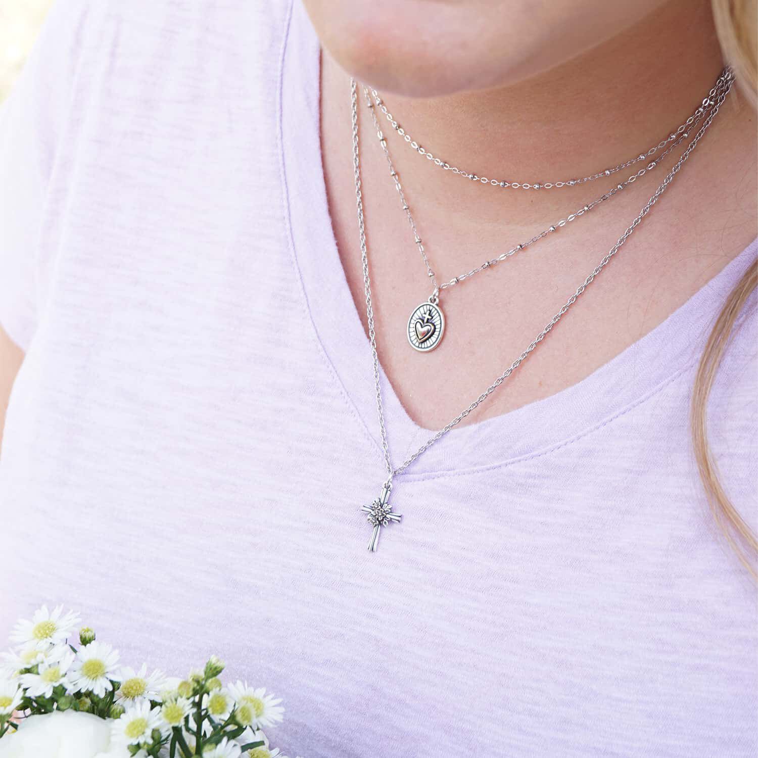 Model wearing layered necklaces featuring sterling silver and bronze faith designs. 