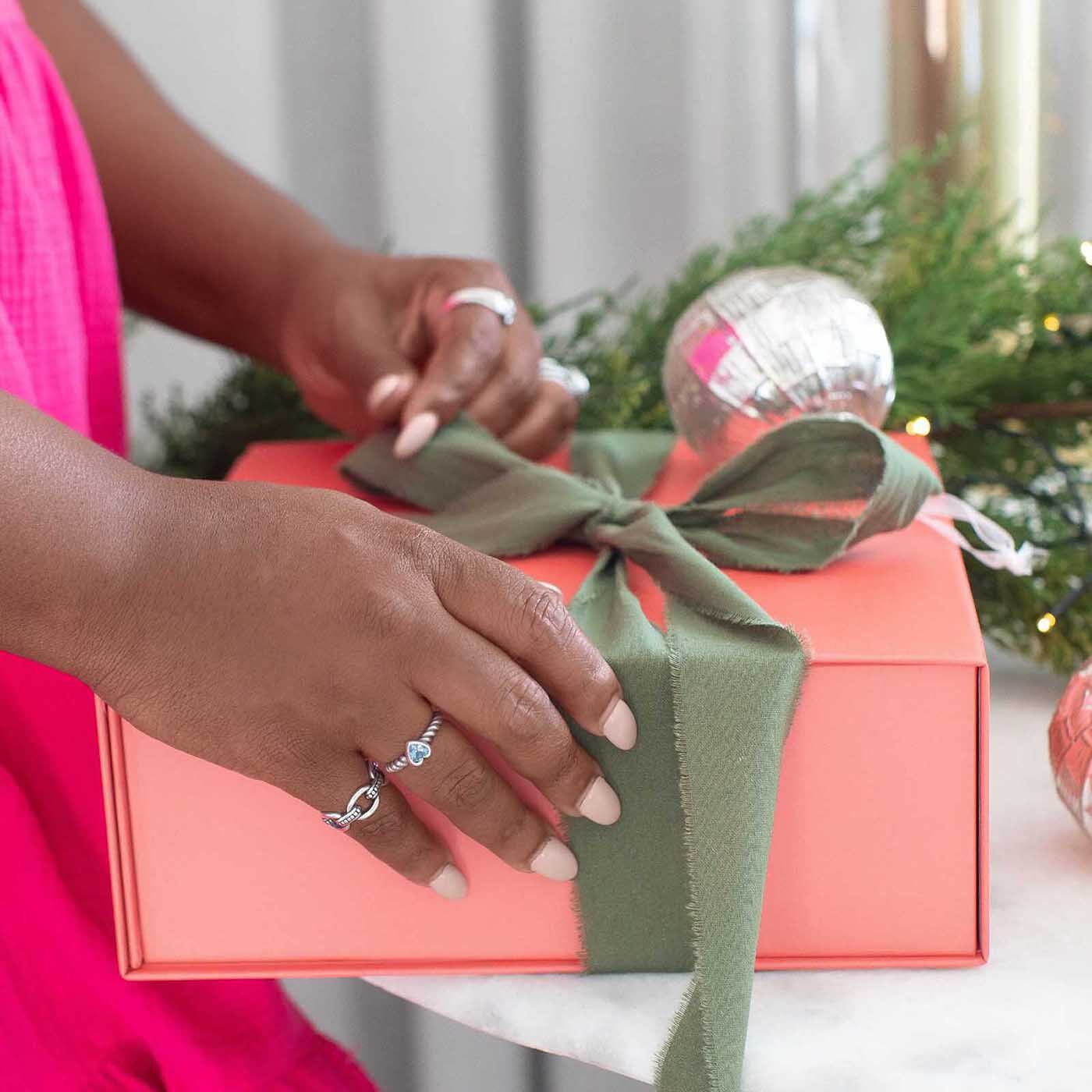 Model wearing sterling silver rings holding a coral gift box with green ribbon