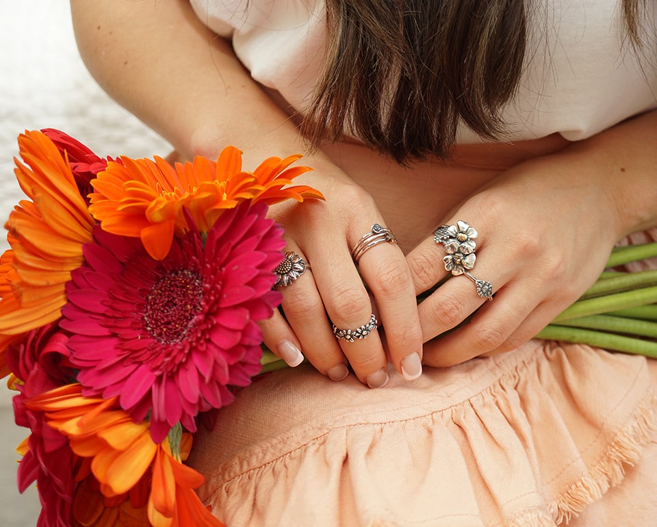 Woman ssitting with hands crossed holding flowers while wearing stacked rings